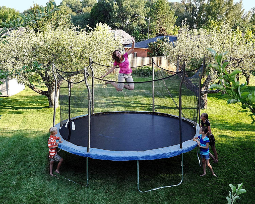 Backyard trampoline fun: a girl jumping while other children watch, surrounded by trees and green lawn